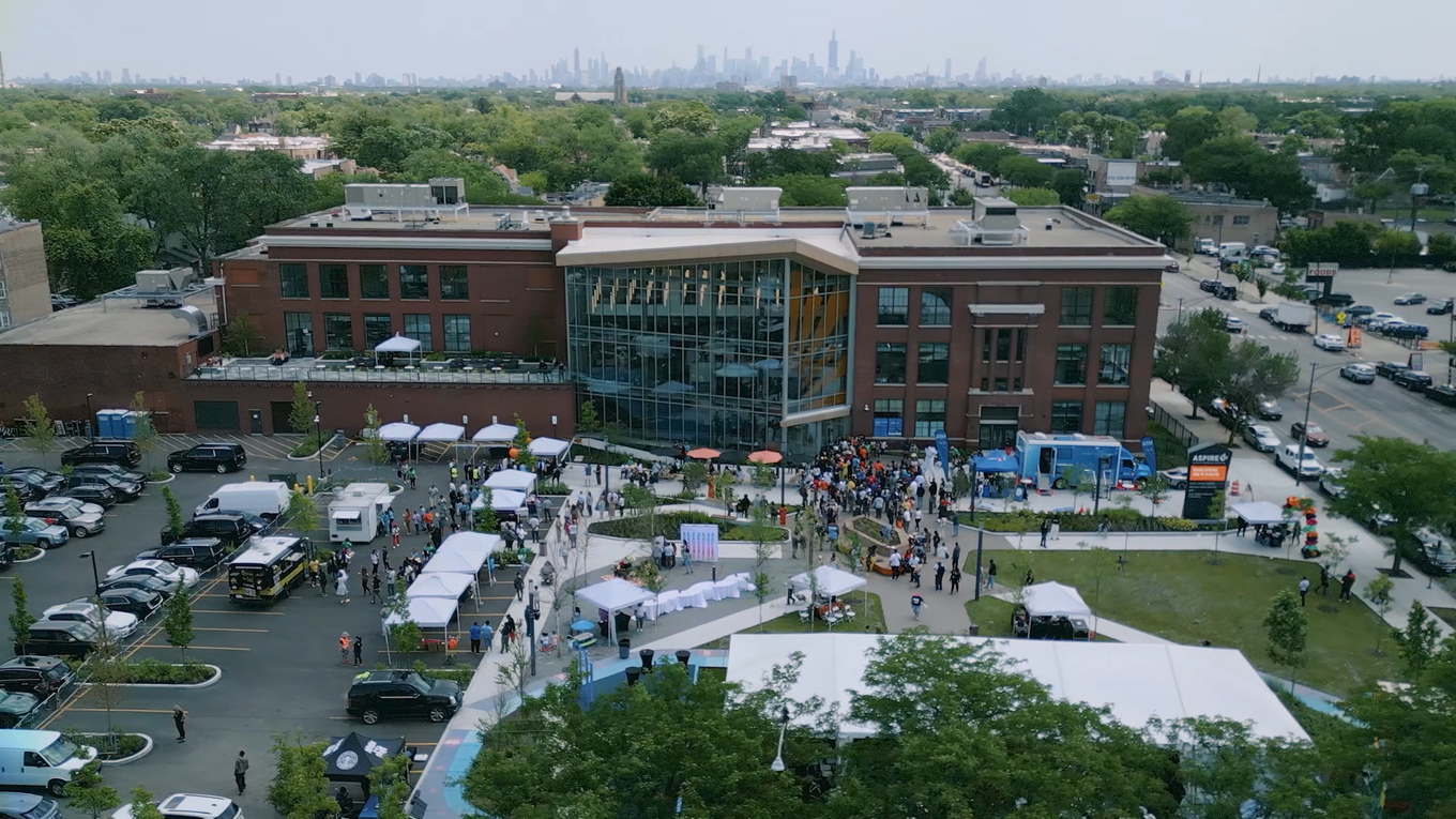 Aerial photograph of a red brick building with a large glass facade during an outdoor event.
