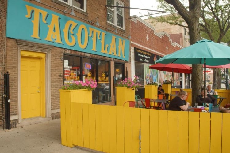 Exterior of Tacotlan restaurant with a yellow fence and outdoor patio seating.