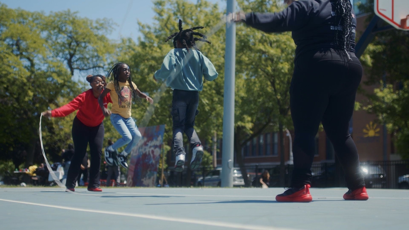 Children playing jump rope on an outdoor court.
