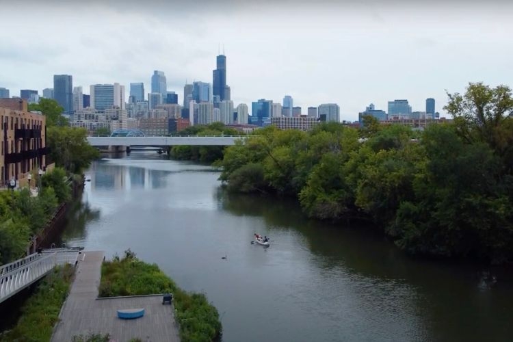 Photograph of a calm river leading toward the Chicago city skyline with a canoe in the water.