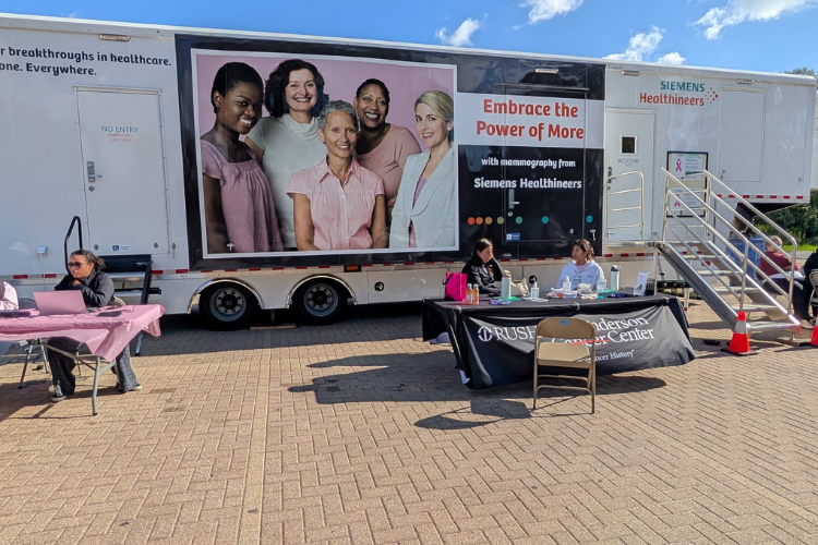 A Siemens Healthineers mobile mammography unit parked outdoors with staff at folding tables.