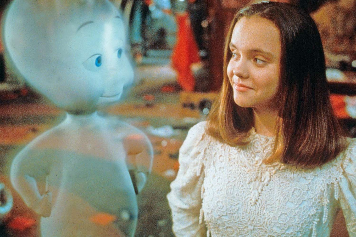 Casper the friendly ghost looks at a smiling young girl in a lacy white dress.