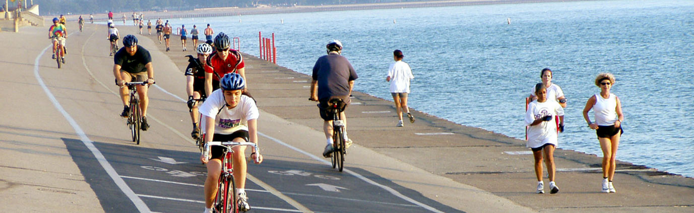 Cyclists and joggers exercise on the Lakefront Trail on a sunny summer day.