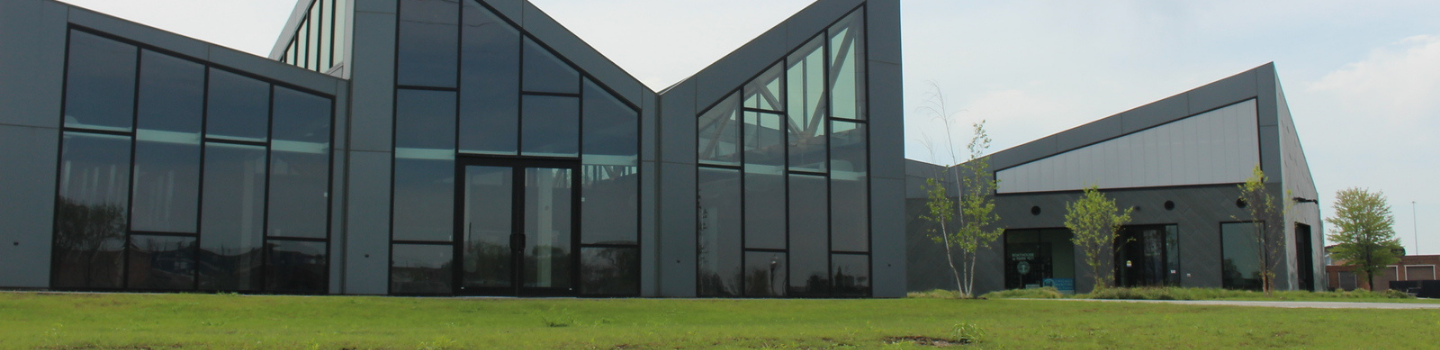 Boathouses.png Modern building with angled glass walls and a grassy lawn.