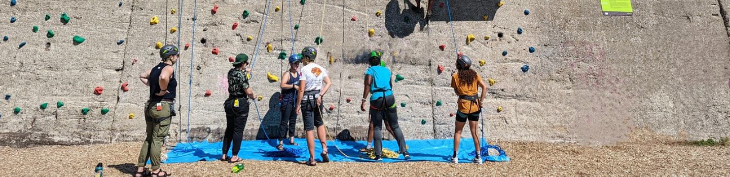 Climbing Walls.png Group of young rock climbers preparing at the base of a climbing wall.