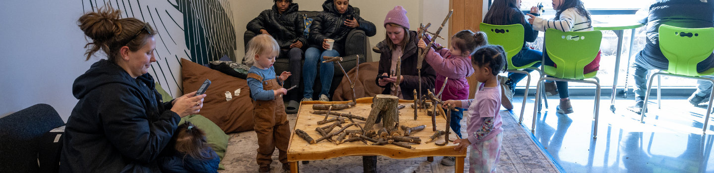 Nature Center.png Children and adults play with sticks at a nature-themed table.