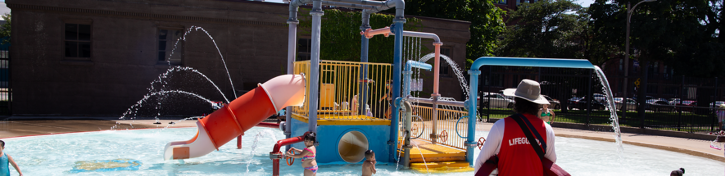 Water Playgrounds.png Children play on a colorful splash pad; a lifeguard watches.