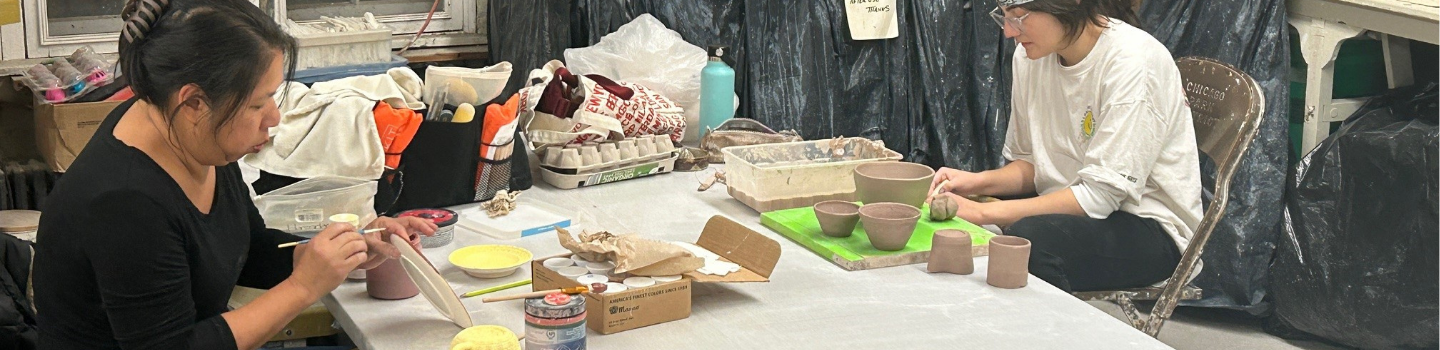 Two people paint pottery at a messy work table.