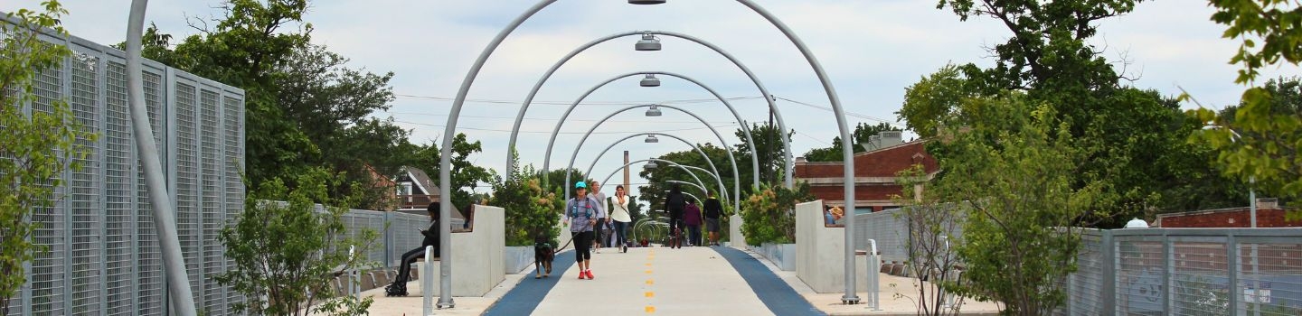 Pedestrians and cyclists on an elevated path with arched lampposts.