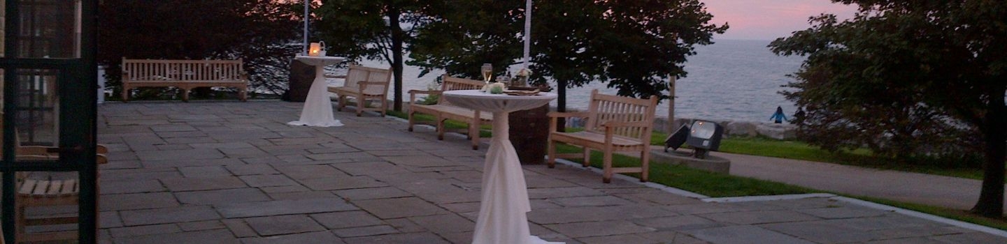 Outdoor patio with cocktail tables, benches, and view of a lake at sunset.
