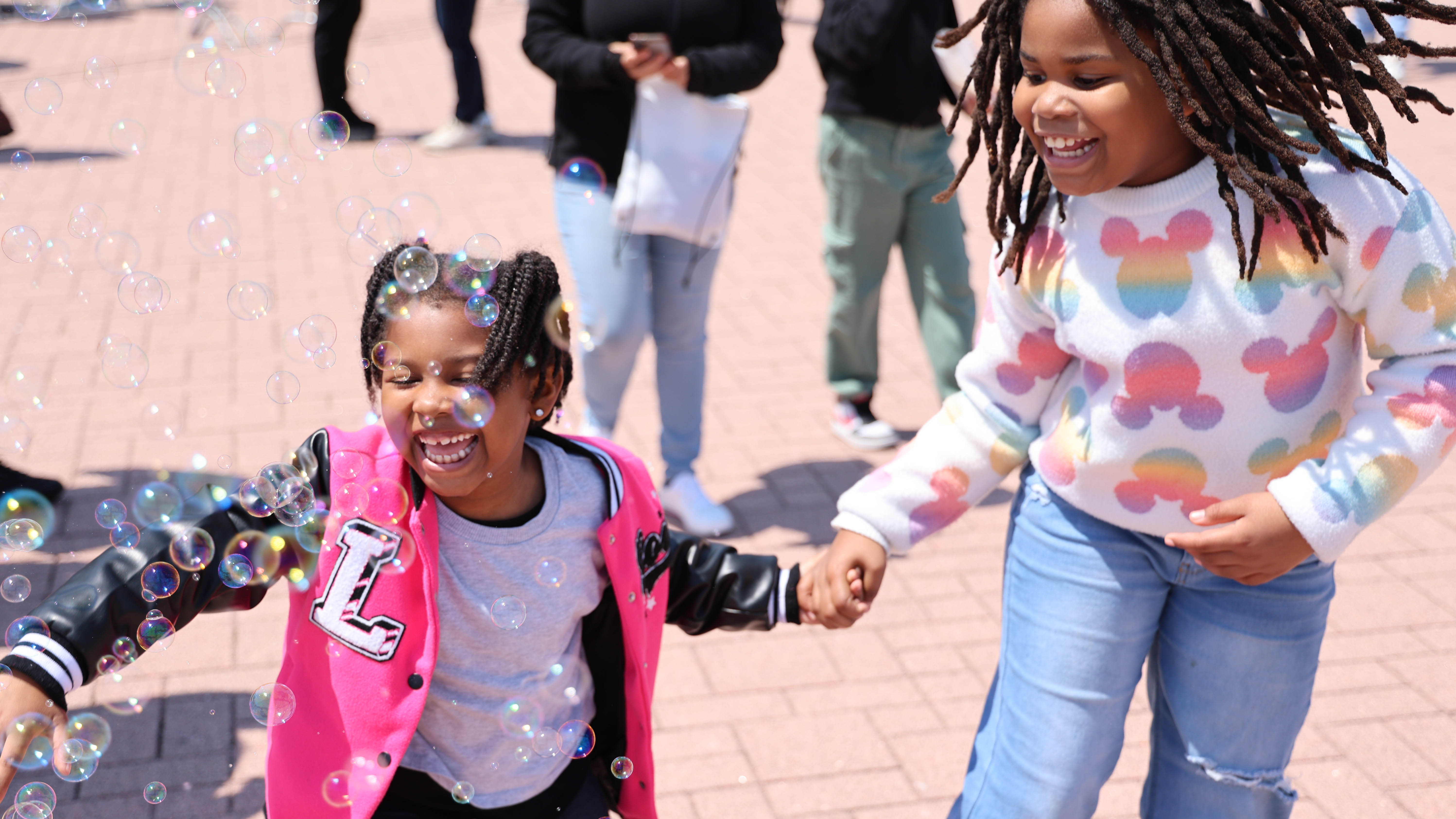 Two smiling children hold hands and play with bubbles.