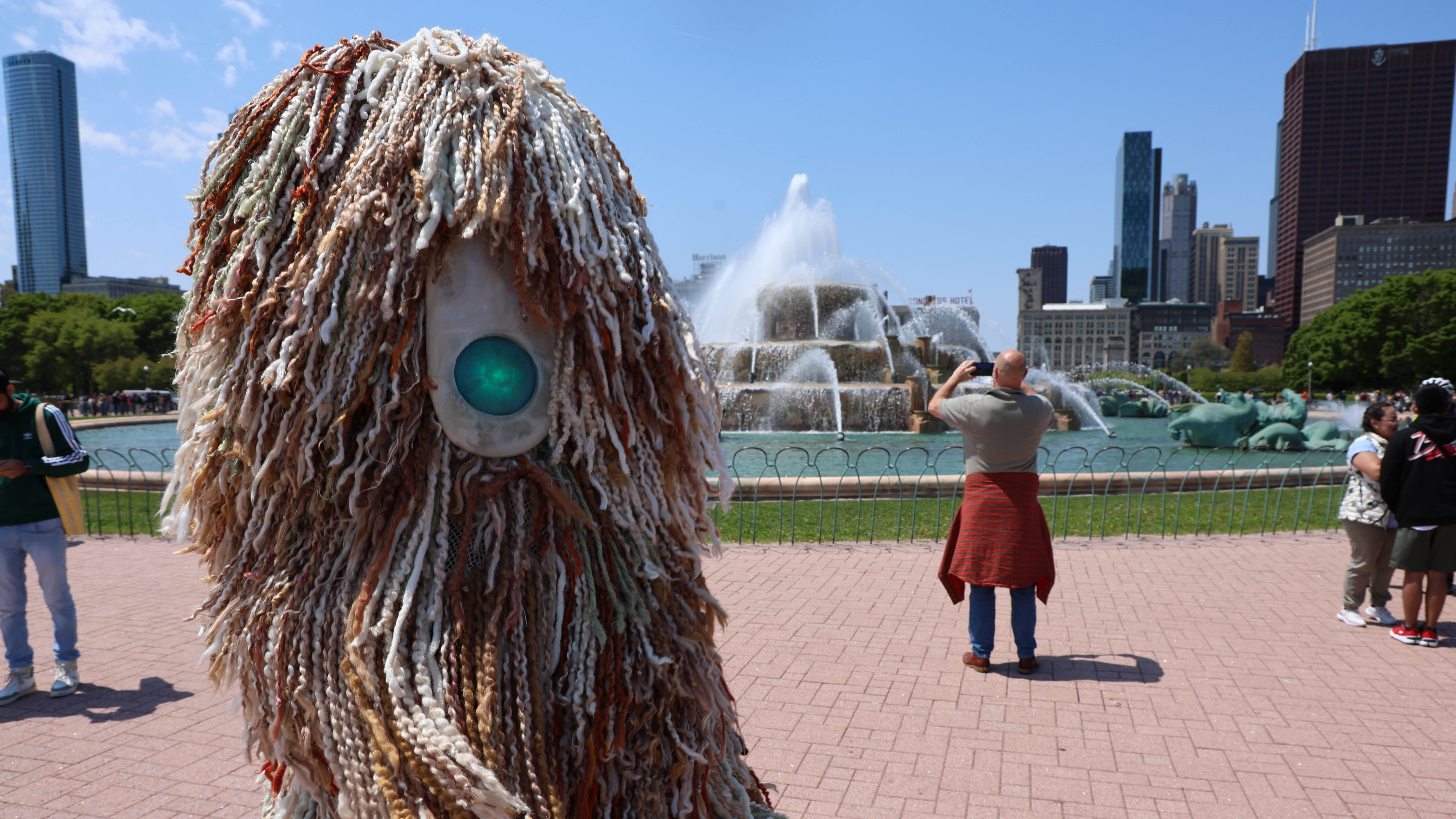Large yarn sculpture with a single green eye, Buckingham Fountain in the background.