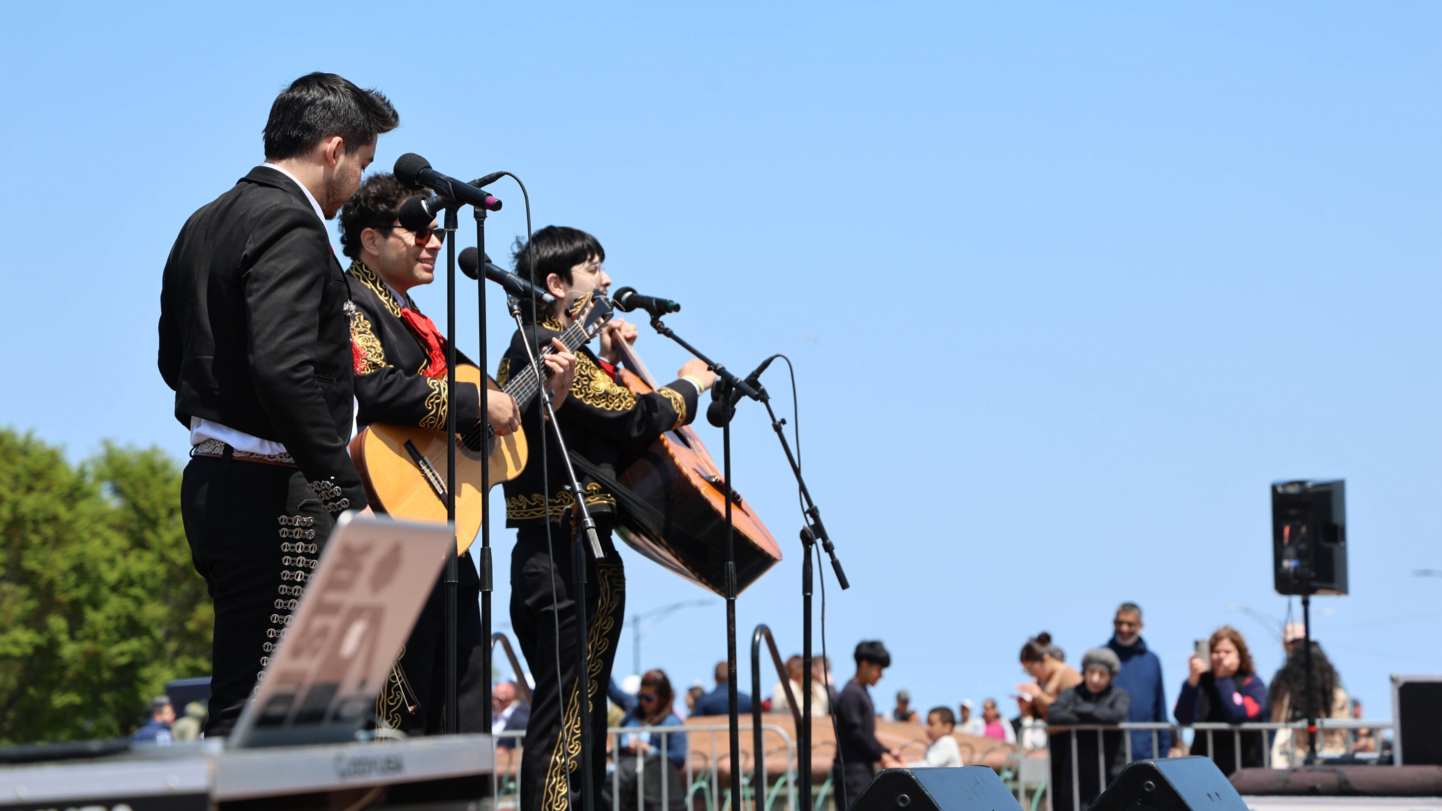 Mariachi band plays on an outdoor stage for a small crowd.