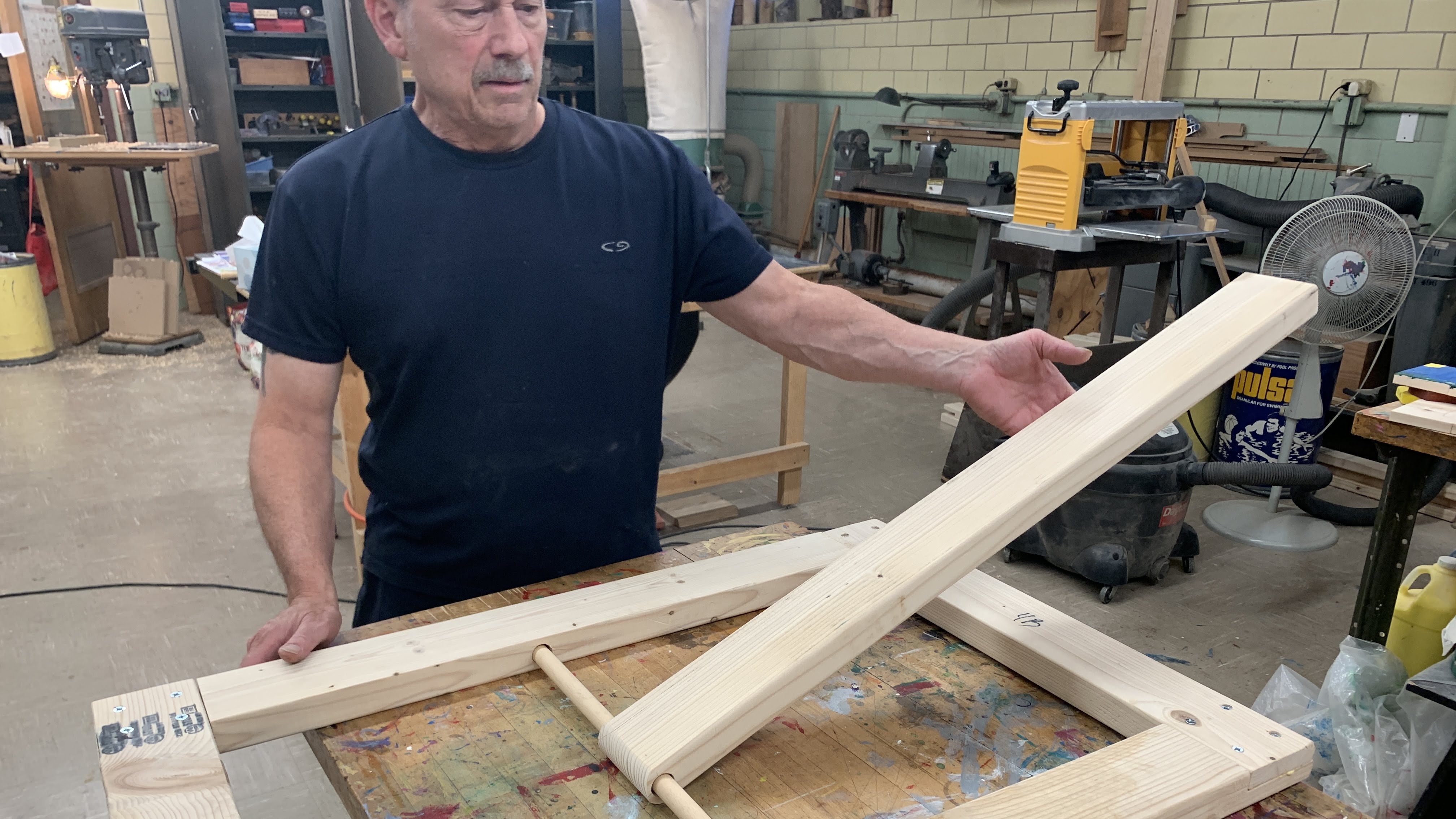 Wooden frame with pivoting arm demonstrates lever action. Man in workshop.