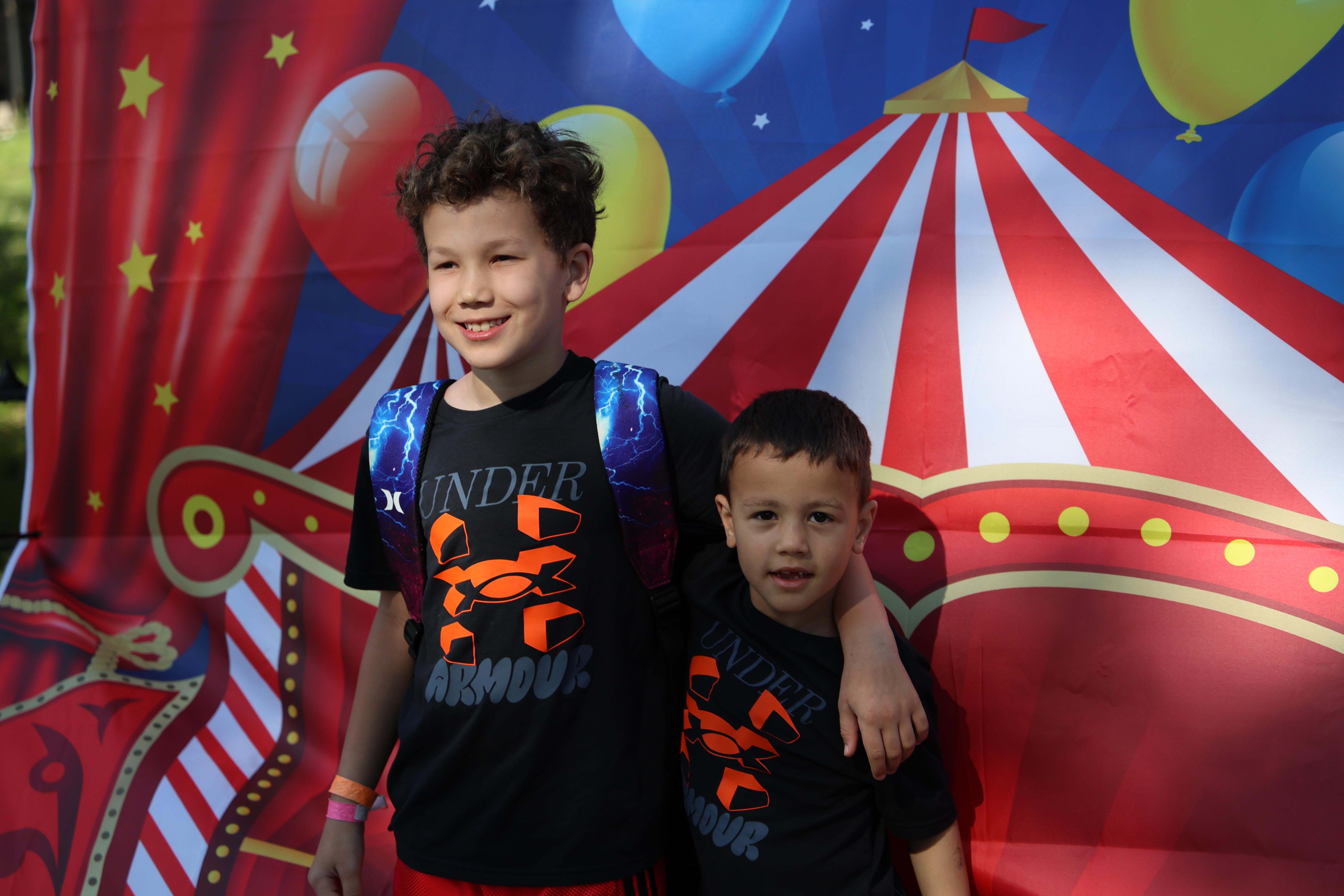 Two smiling boys pose in front of a circus-themed backdrop.