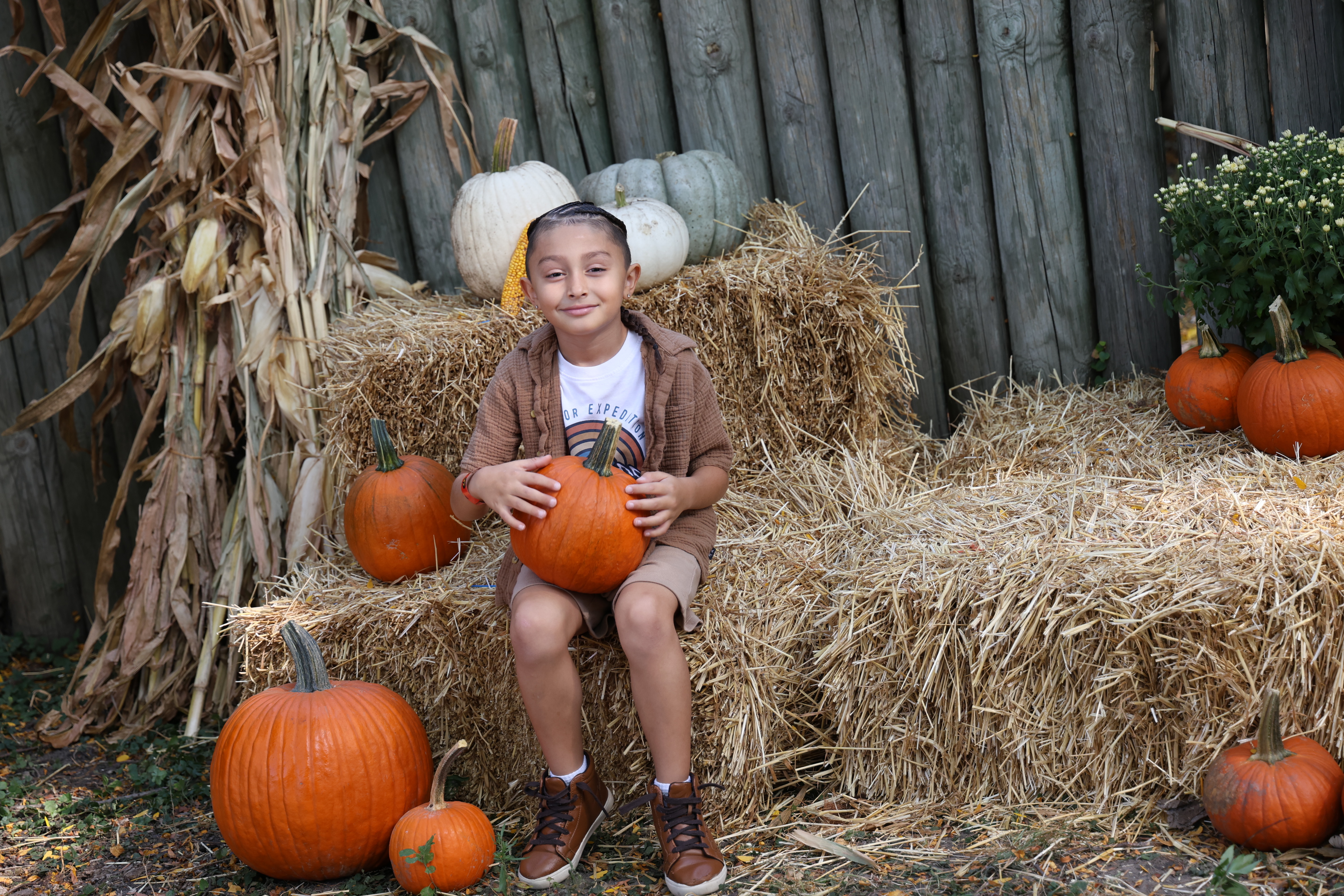 Boy with a pumpkin, sitting on hay bales, smiling.
