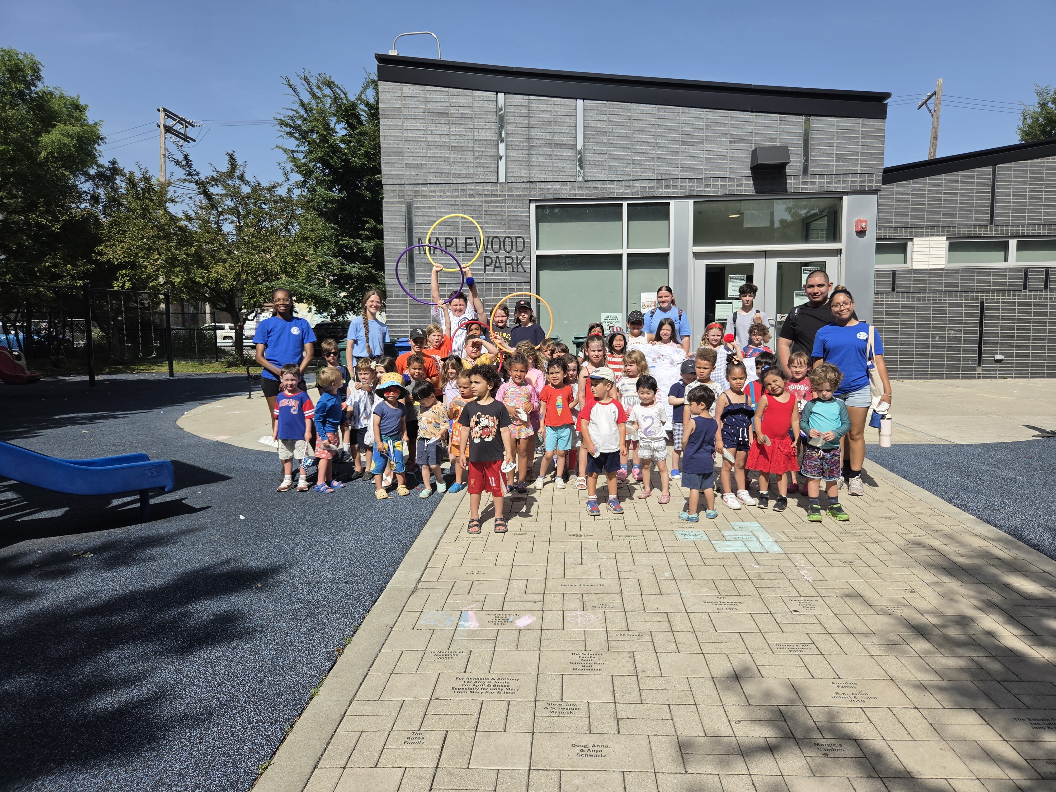 Group of children and adults posing for a photograph in front of the Maplewood Park building.