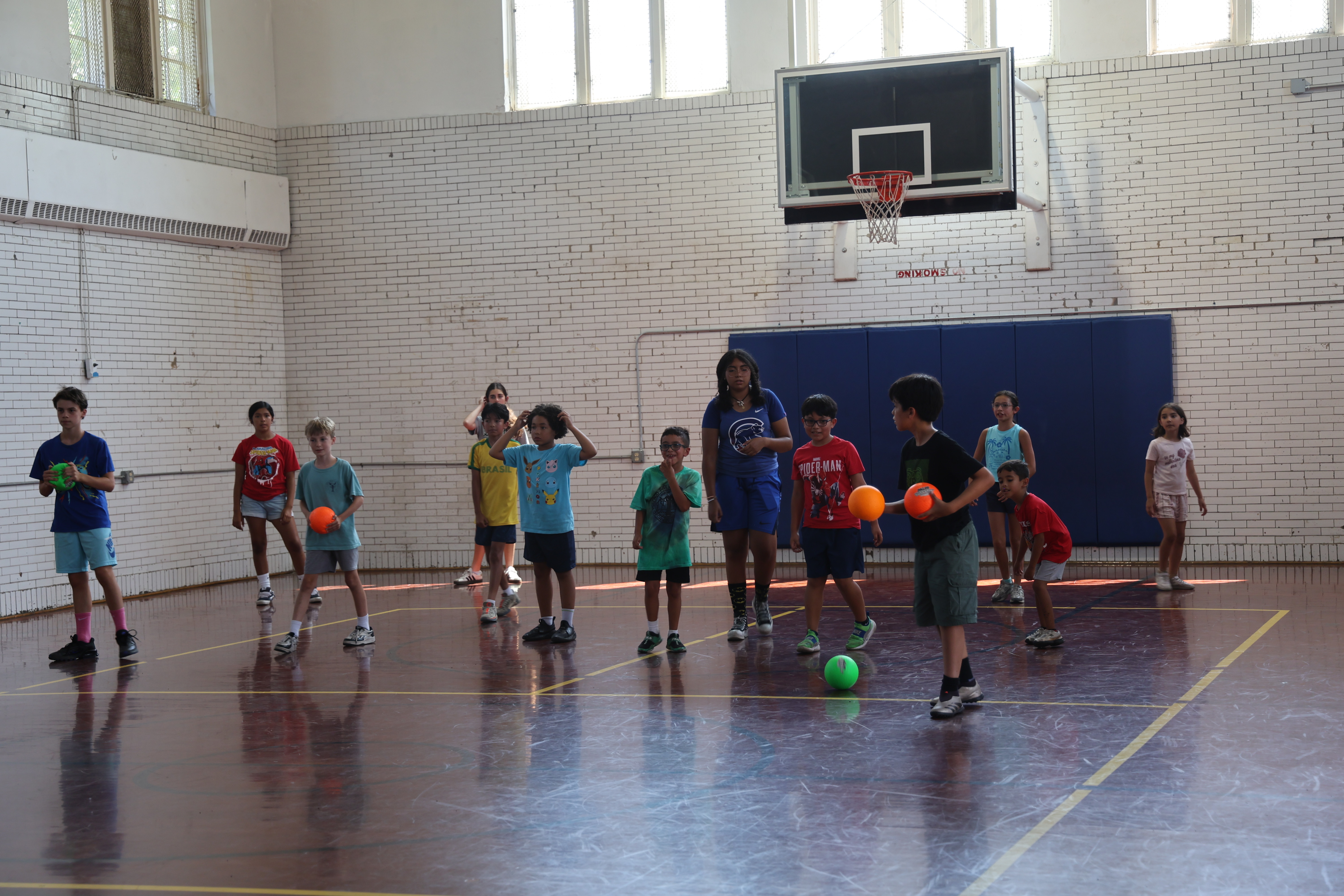 Group of children and a counselor playing with balls in a school gymnasium.