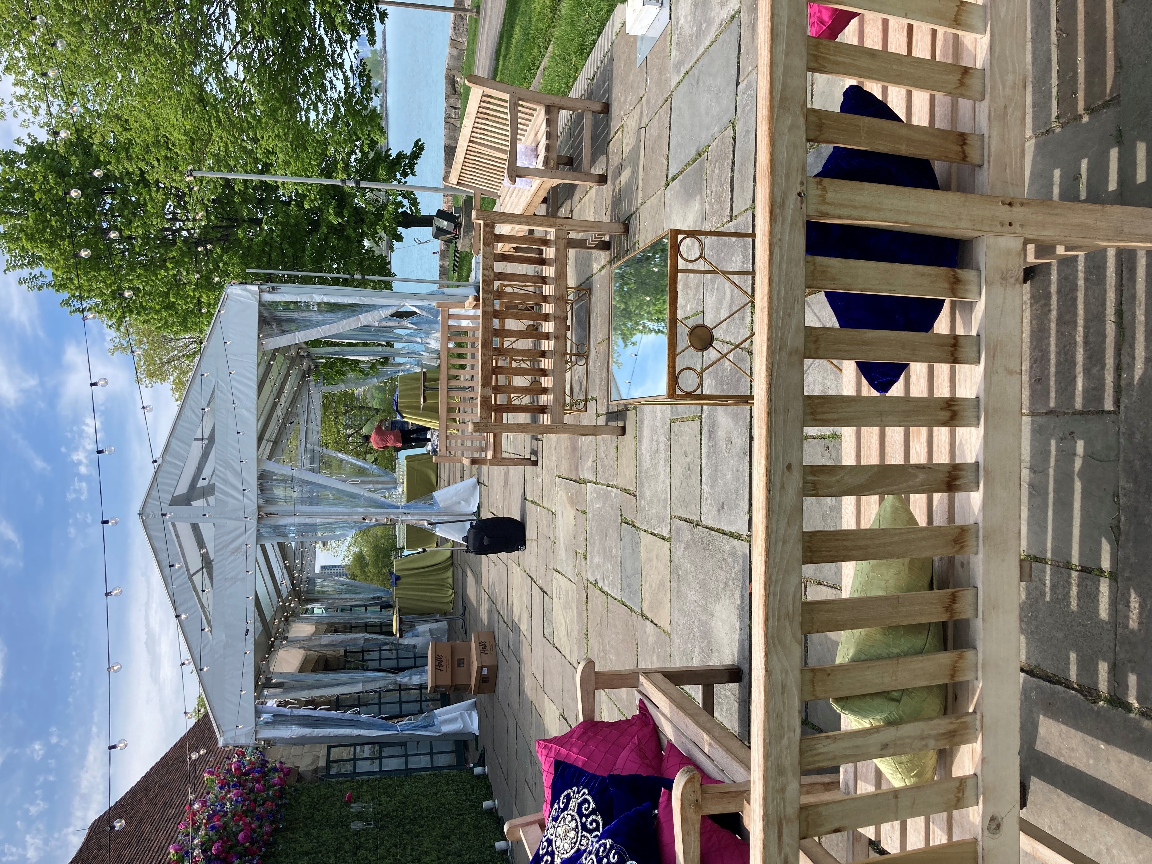 Outdoor event setup with wooden benches, colorful cushions, string lights, and a tented area.