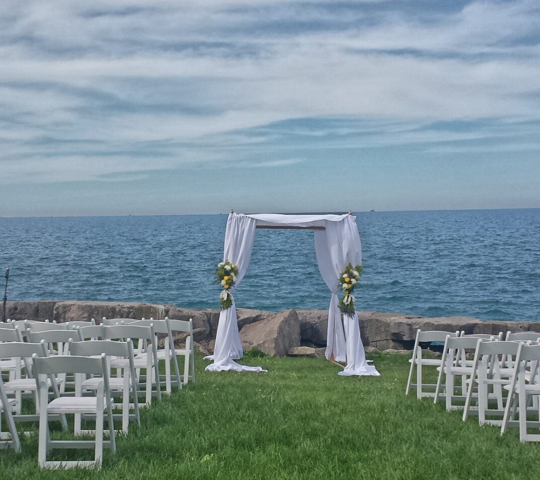 Outdoor wedding setup with white chairs and floral-decorated arch overlooking a lake.