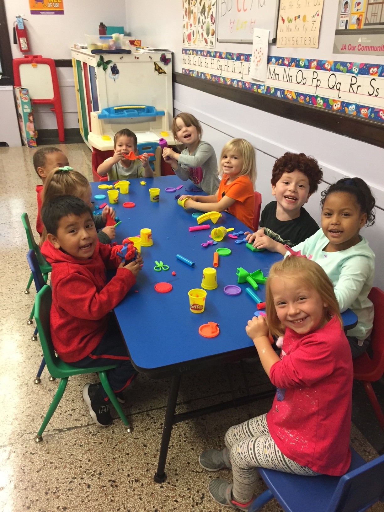 Children happily play with Play-Doh at a blue table.