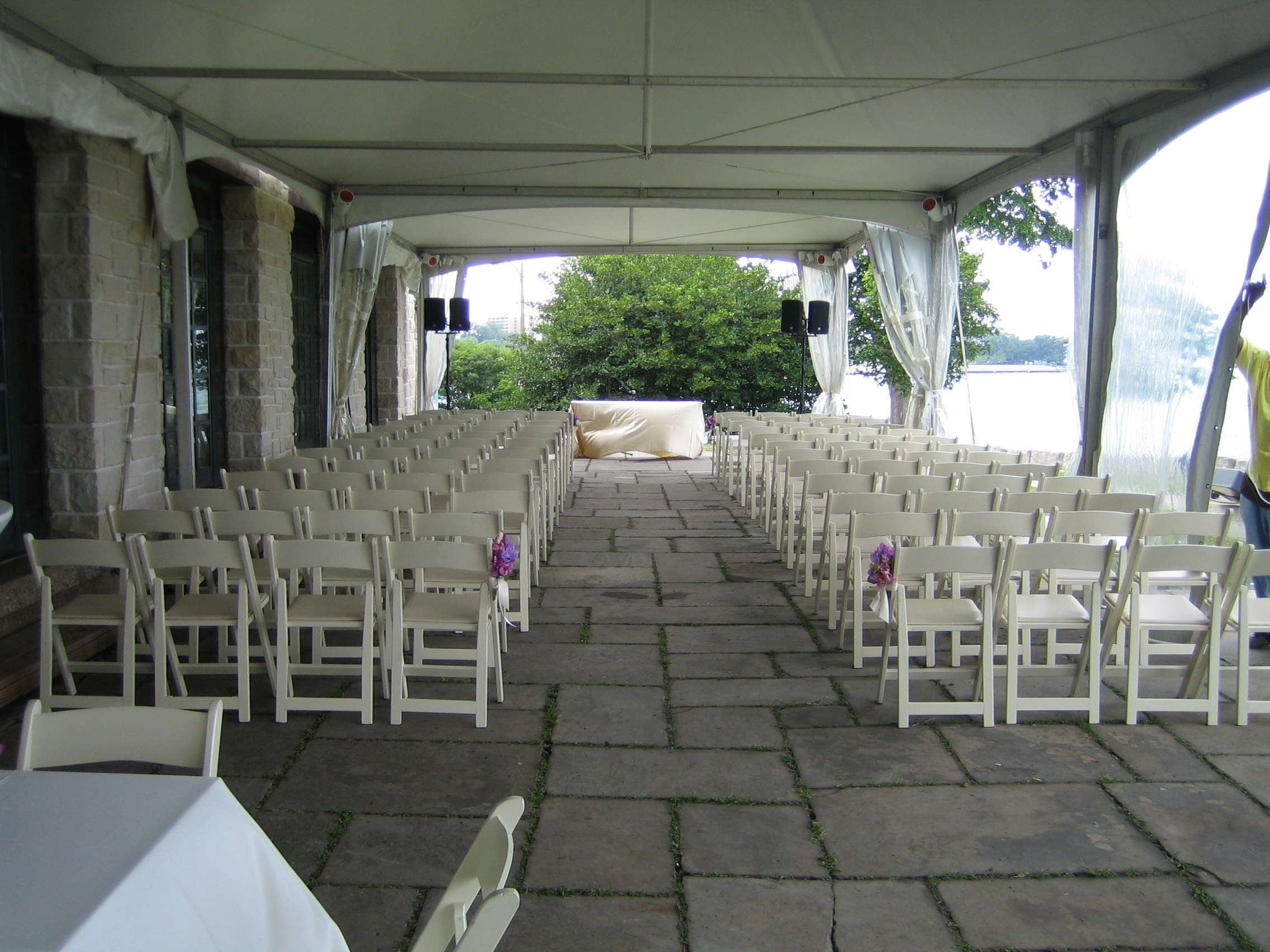 Outdoor wedding venue set up with rows of white folding chairs under a canopy.