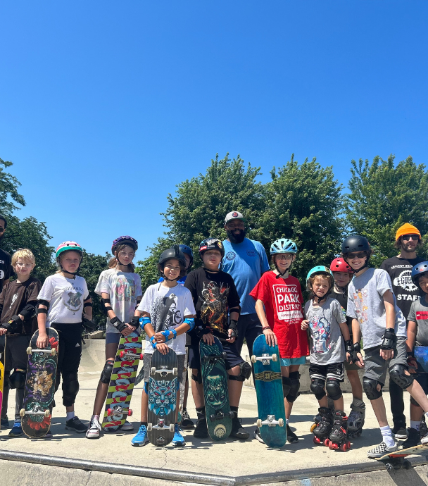 Group of kids and adults with skateboards and safety gear at a skate park.