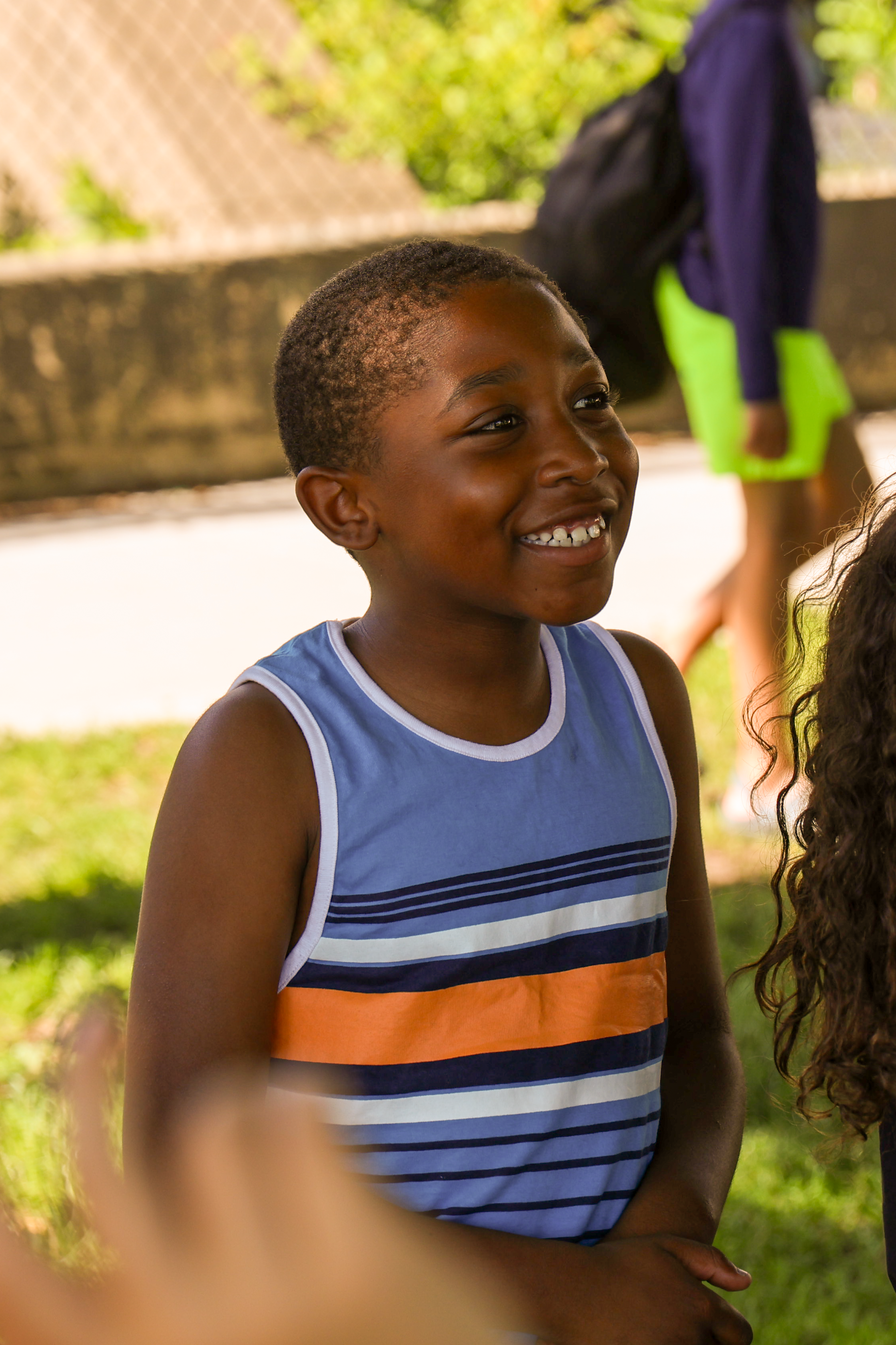 Smiling boy wearing a blue and orange striped tank top.