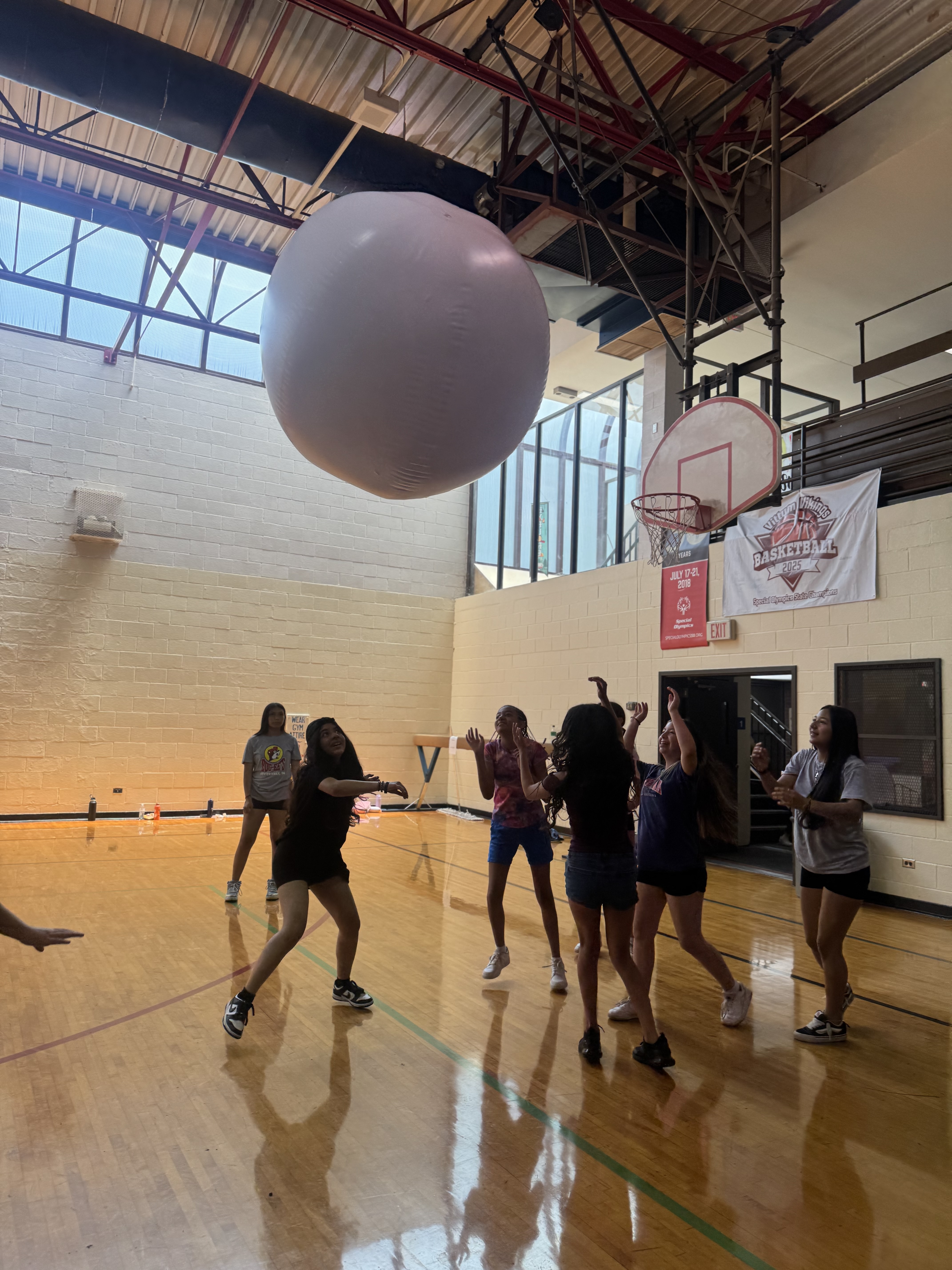 Teenagers playing with a large white ball in a gymnasium.