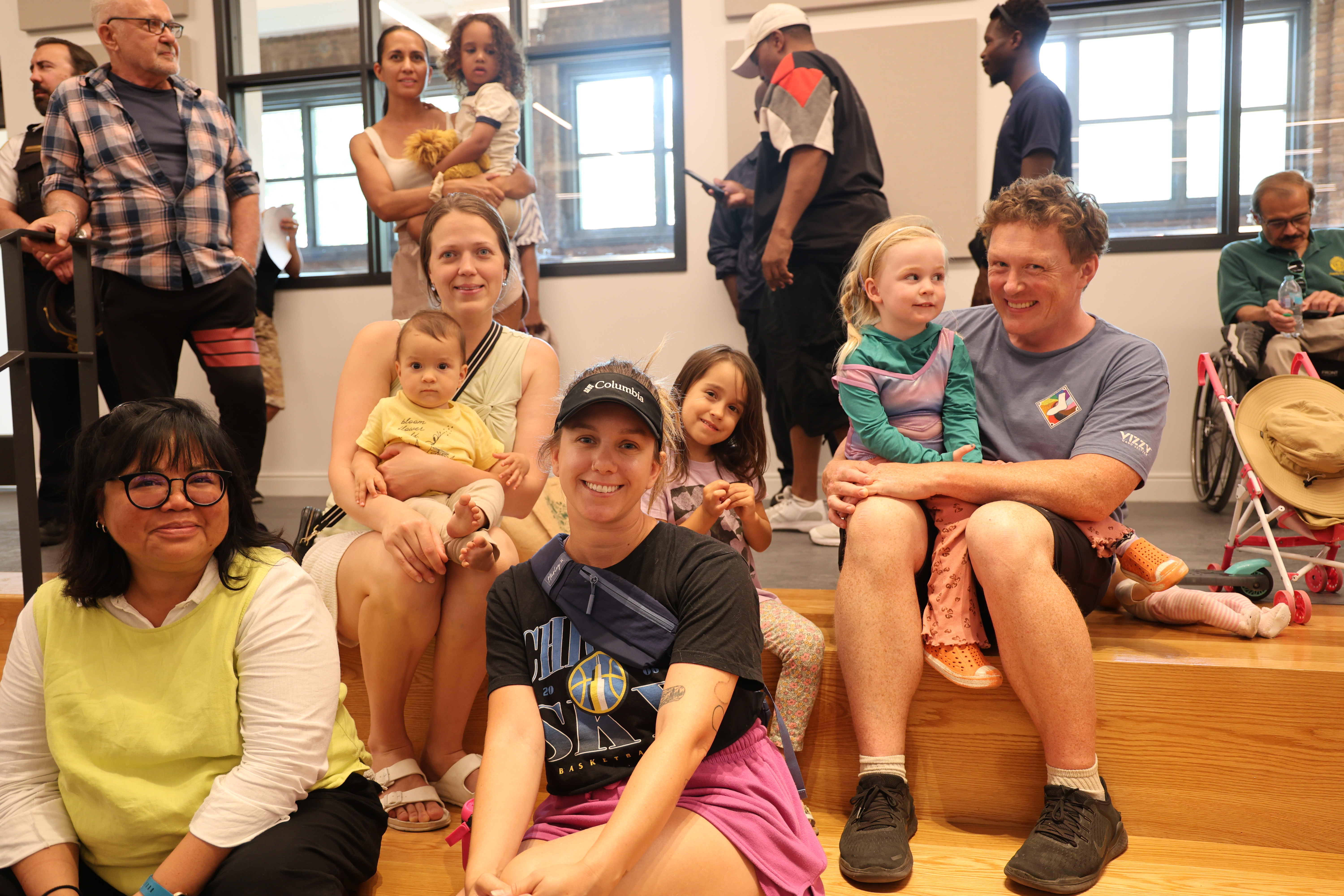 Families with young children sit on wooden steps in a community space.