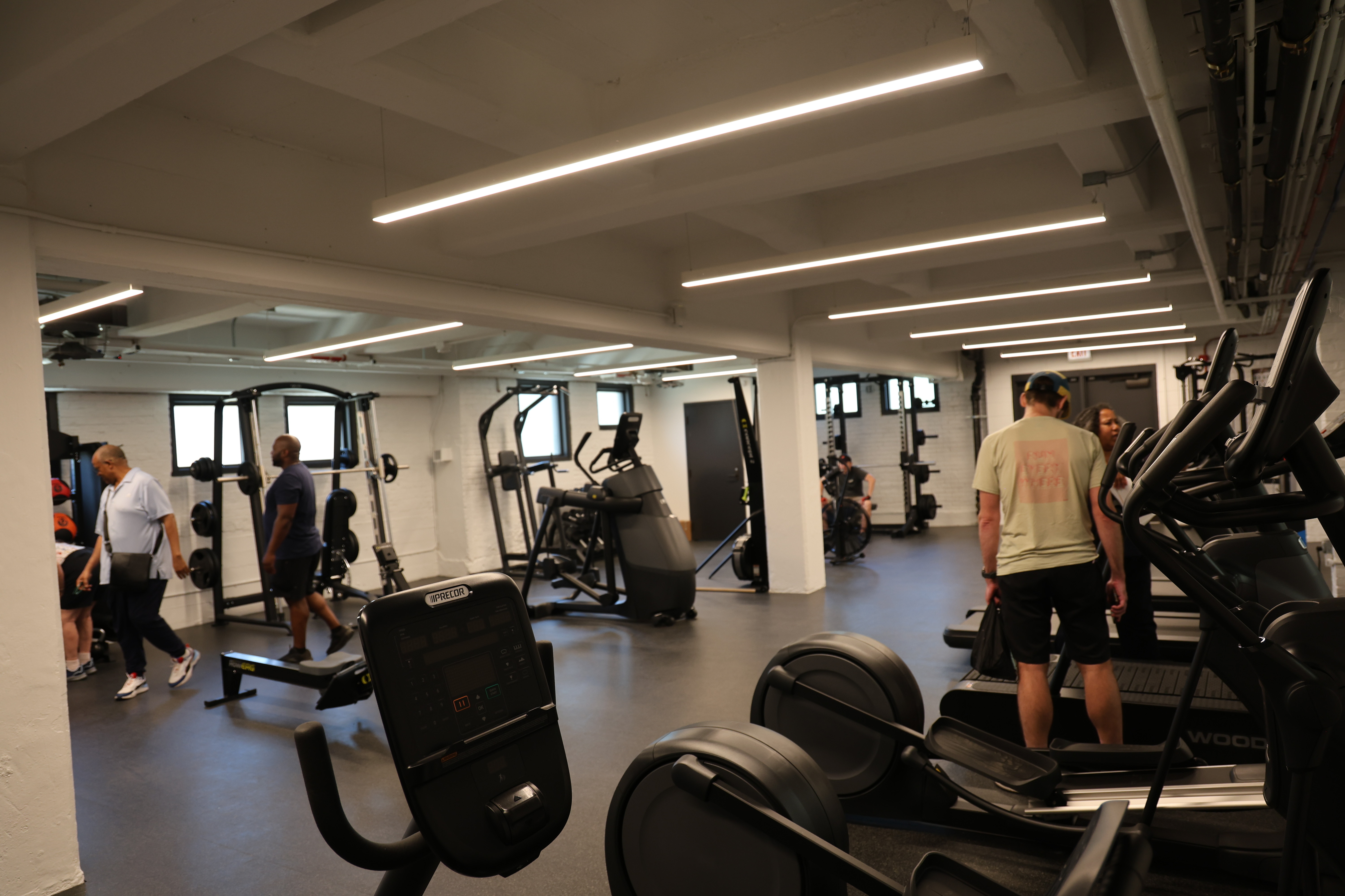 People work out in a brightly lit gym with various exercise equipment.