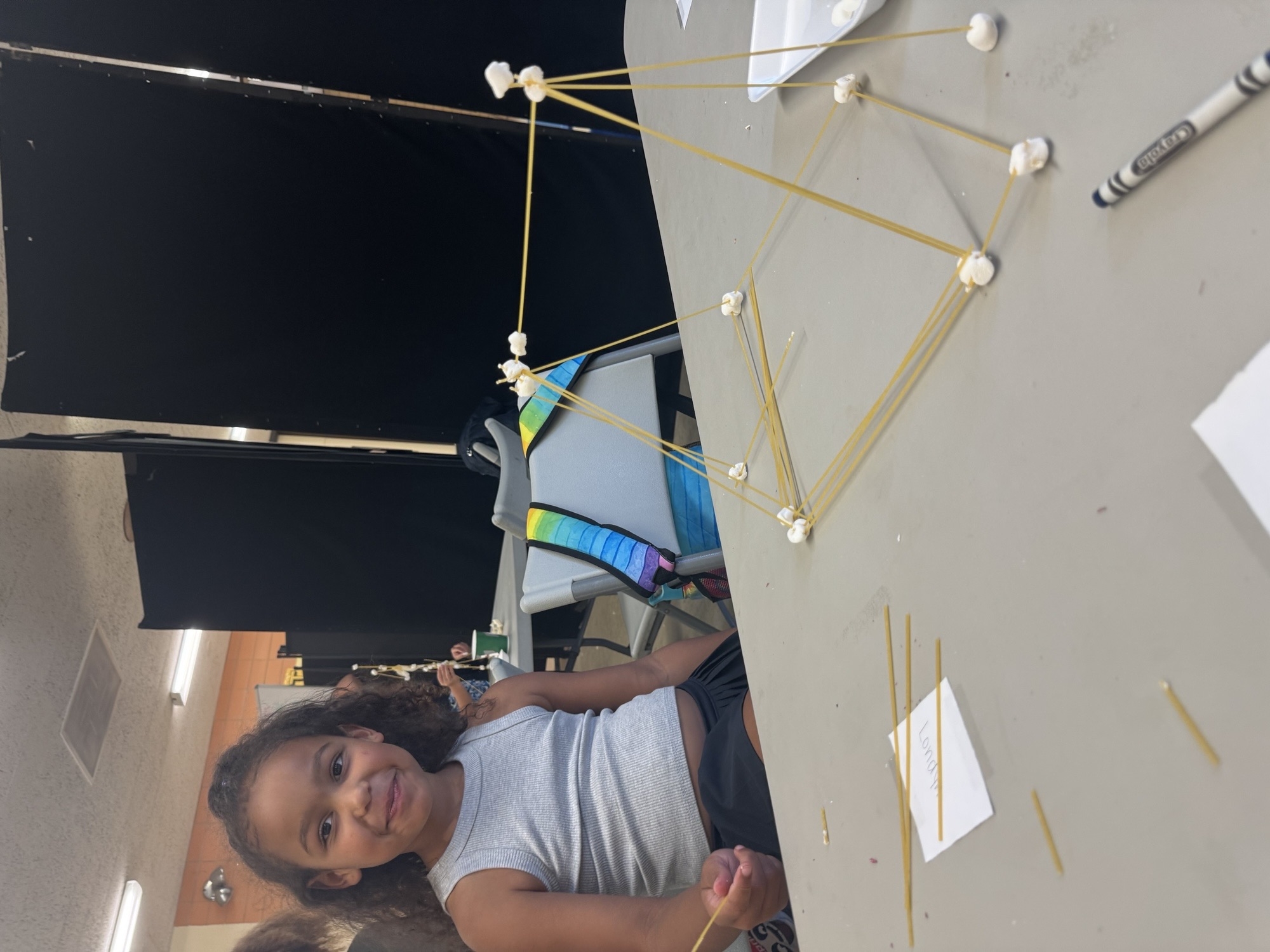 A girl building a marshmallow spaghetti tower.