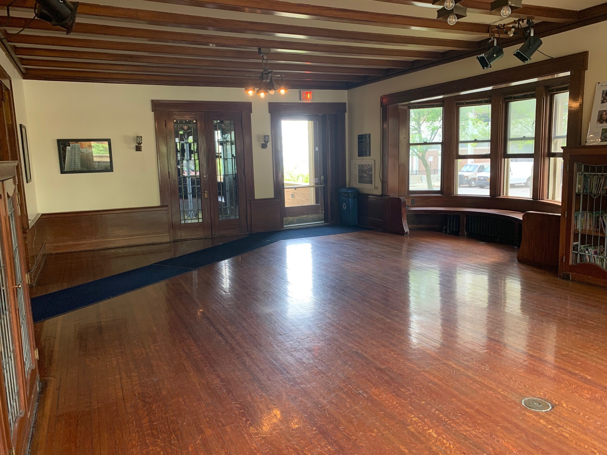 Spacious room with polished hardwood, dark wood beams, bay windows, and bright exit door.