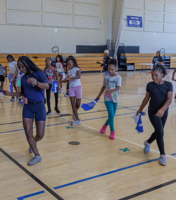 Girls and adults holding blue cloths during an activity in a bright gymnasium at Fosco Park..
