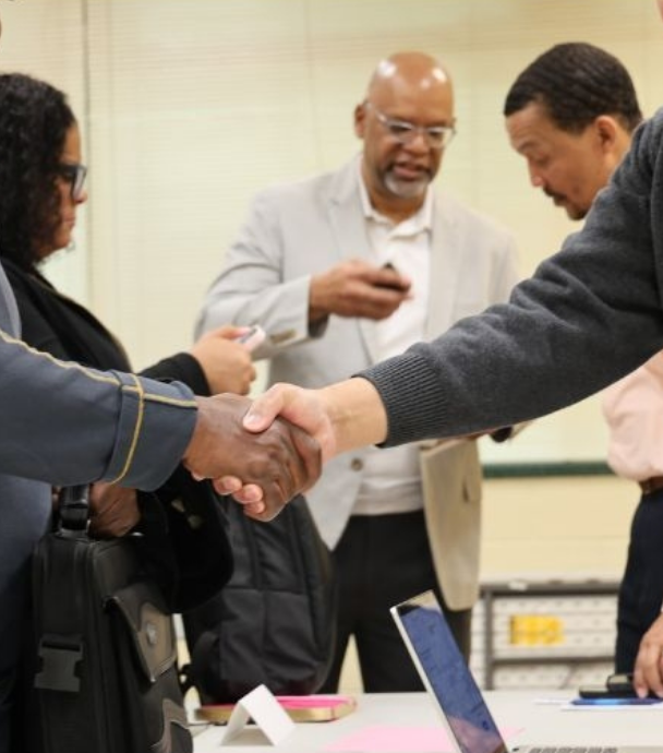 Two people shaking hands at a professional gathering with others in the background.