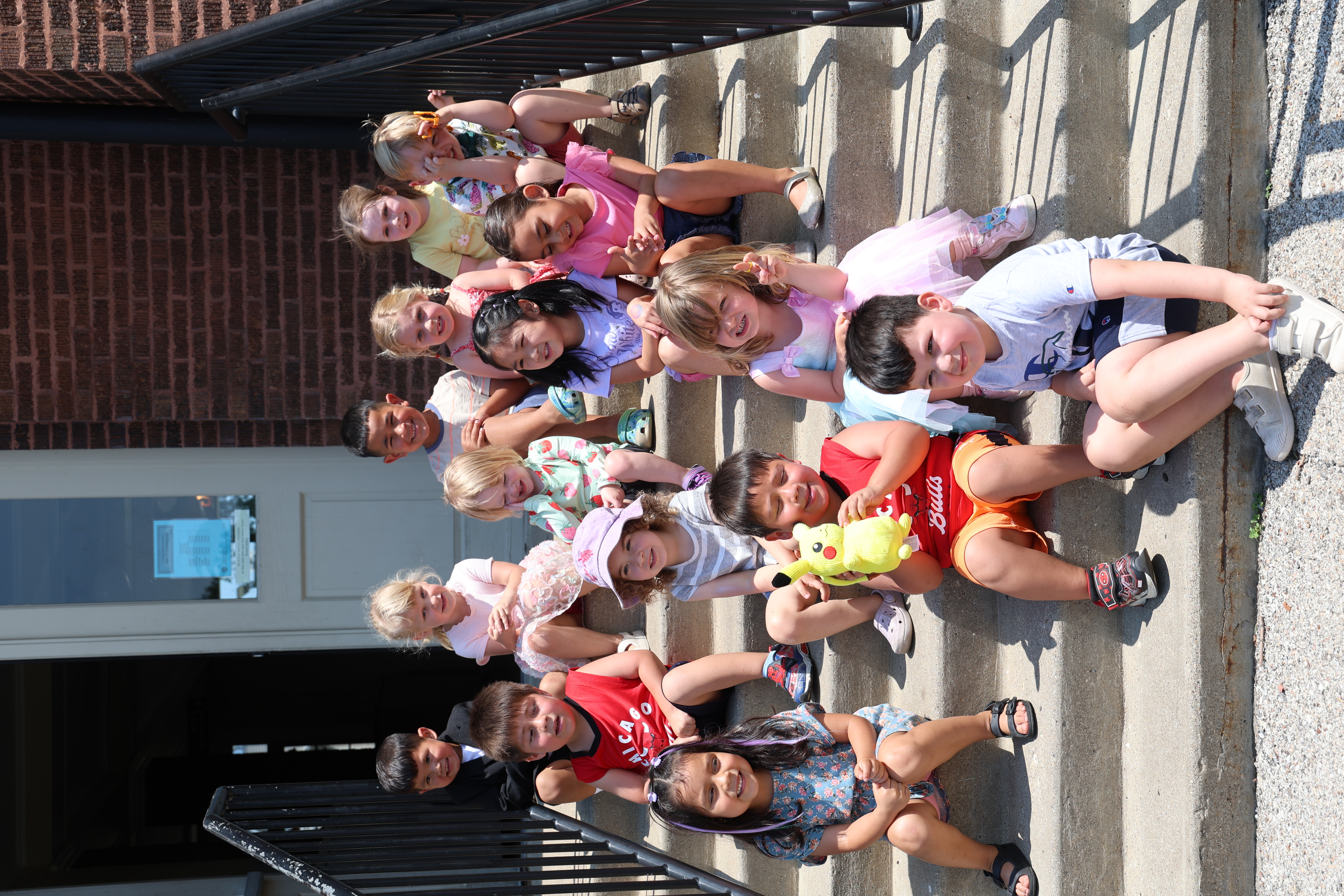 A group of diverse children sitting on concrete school steps, with one holding a Pikachu plush.